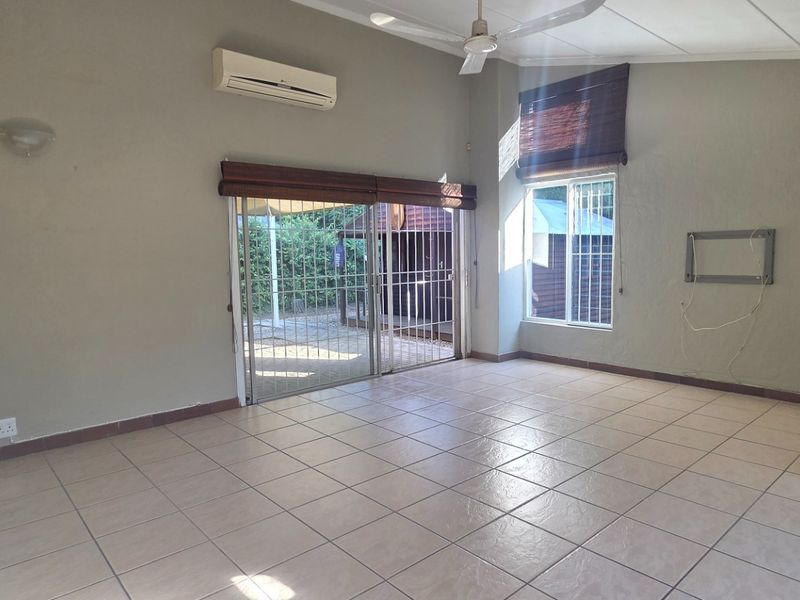 Spacious, empty living area featuring tiled floors, a ceiling fan, split-system air conditioning, and direct access to the outdoor area via sliding glass doors.