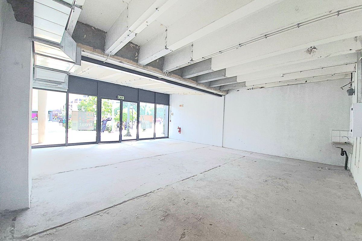 An open-plan retail space featuring an exposed concrete ceiling, large glass storefront, and a basic wall-mounted sink, currently in shell condition.