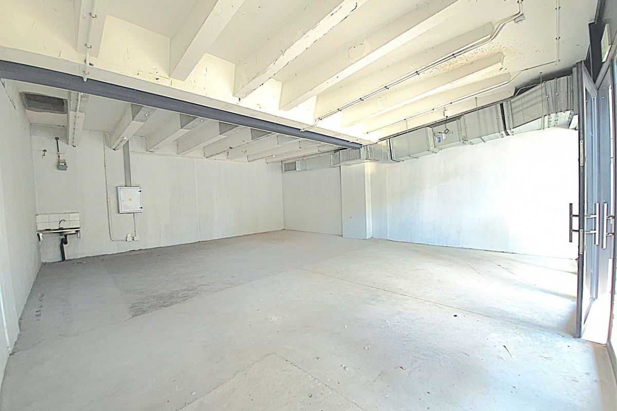 An empty, industrial-style utility space featuring exposed ceiling beams, HVAC ducting, a concrete floor, and a wall-mounted utility sink.