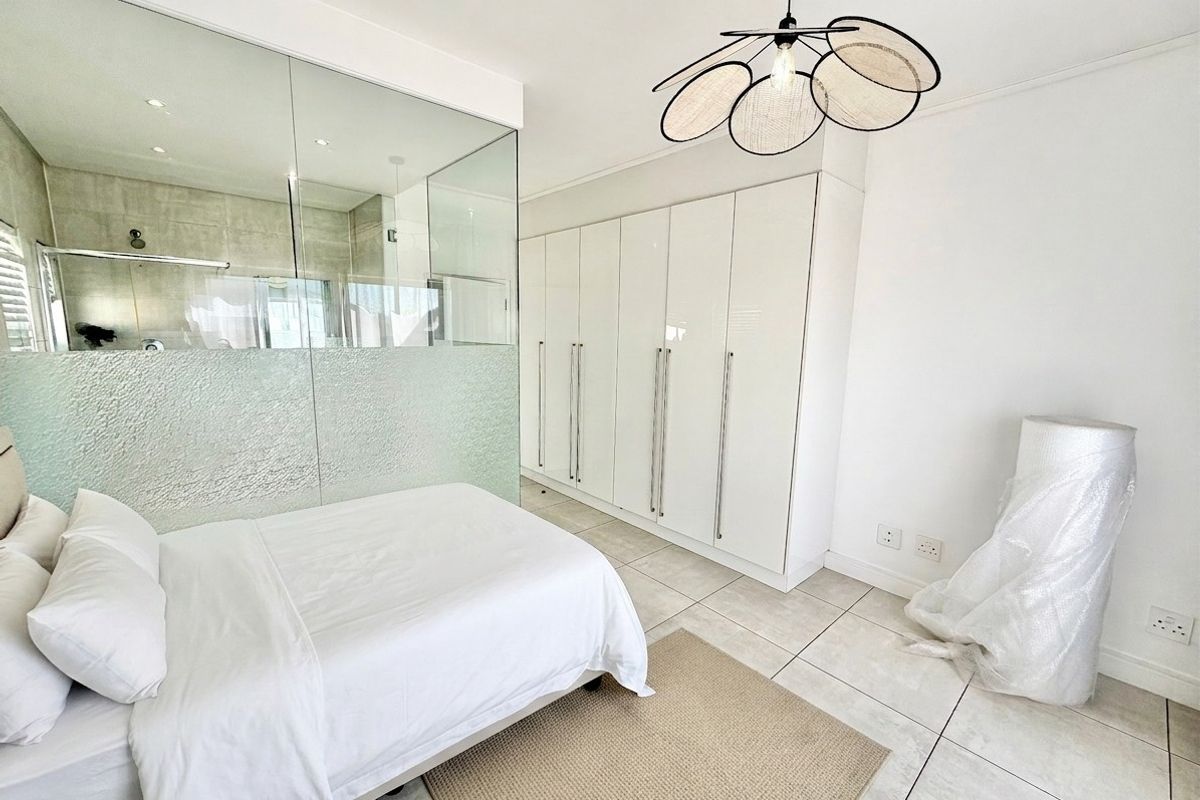 Modern bedroom featuring sleek built-in cupboards, tiled flooring, and a contemporary glass partition wall separating the en-suite bathroom area.