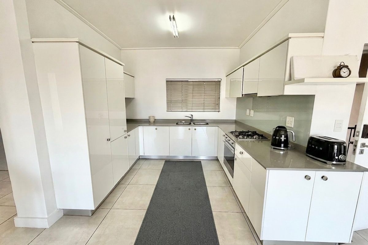 Modern U-shaped kitchen featuring white high-gloss cabinetry, stone countertops, integrated gas hob, built-in oven, and neutral tiled flooring.