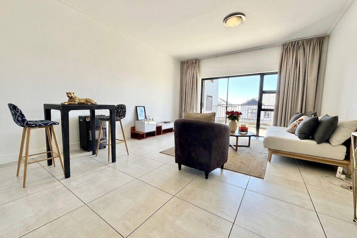 A bright and open living area featuring large format floor tiles and a sliding glass door leading to an outdoor balcony.