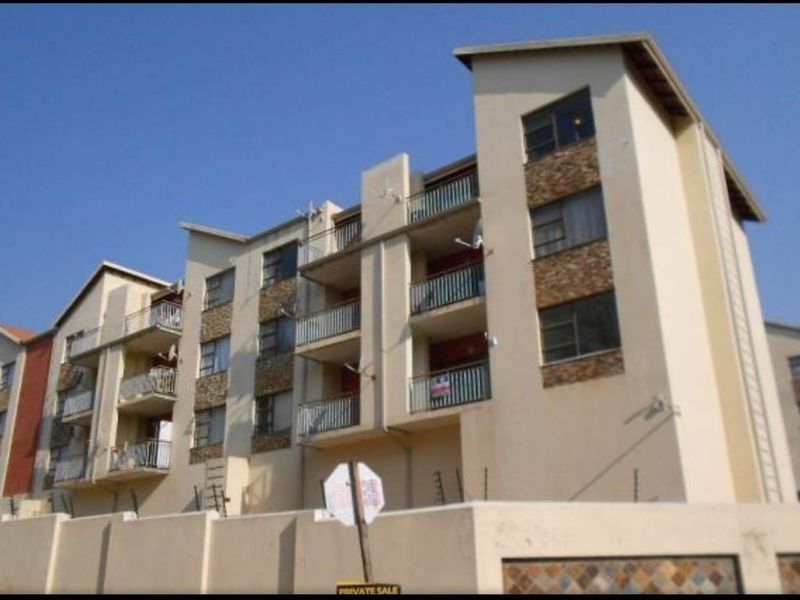 Exterior view of a multi-story apartment complex featuring balconies, stone cladding accents, and a secure perimeter wall with electric fencing.