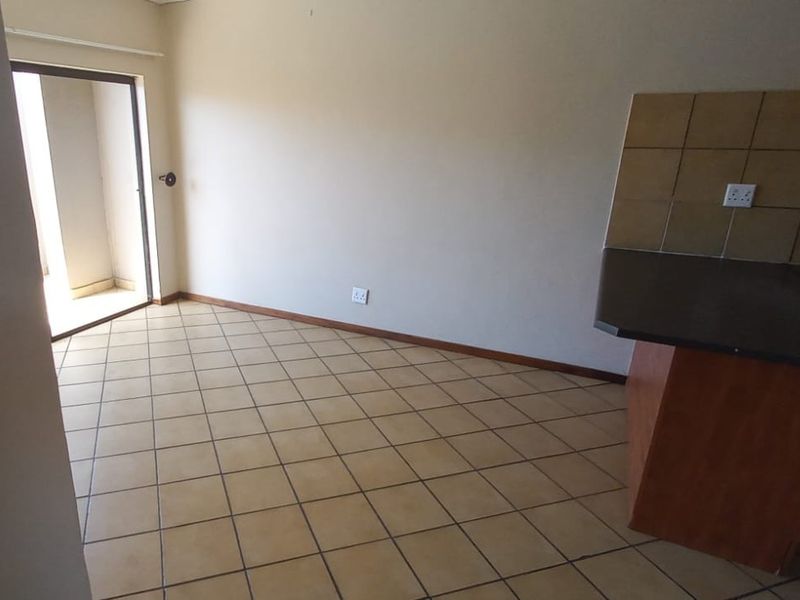 An empty open-plan living and kitchen area featuring tiled flooring, built-in cabinetry, and a sliding door leading to an outdoor space.