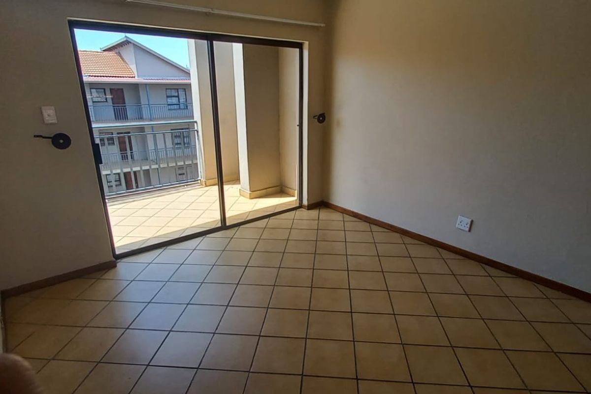 An empty living room featuring tiled flooring and a large sliding glass door providing access to an outdoor balcony area.