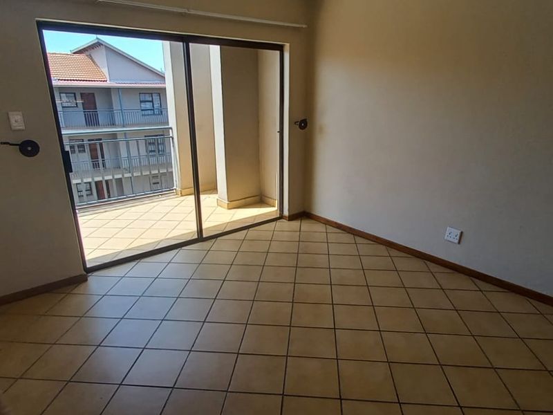 An empty living room featuring tiled flooring and a large sliding glass door providing access to an outdoor balcony area.