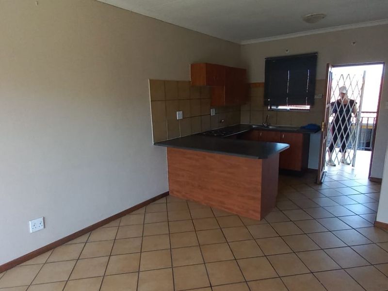 Open-plan living area featuring a functional kitchen with built-in cabinetry, laminate countertops, and tiled flooring, leading to an exterior access point.