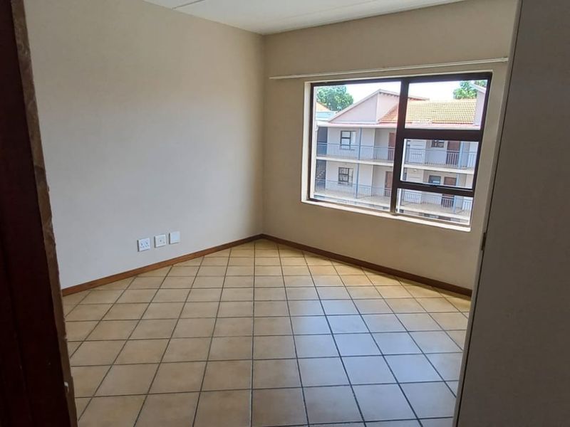An empty bedroom featuring tiled flooring and a large window with an aluminium frame, offering a neutral space ready for personalization.