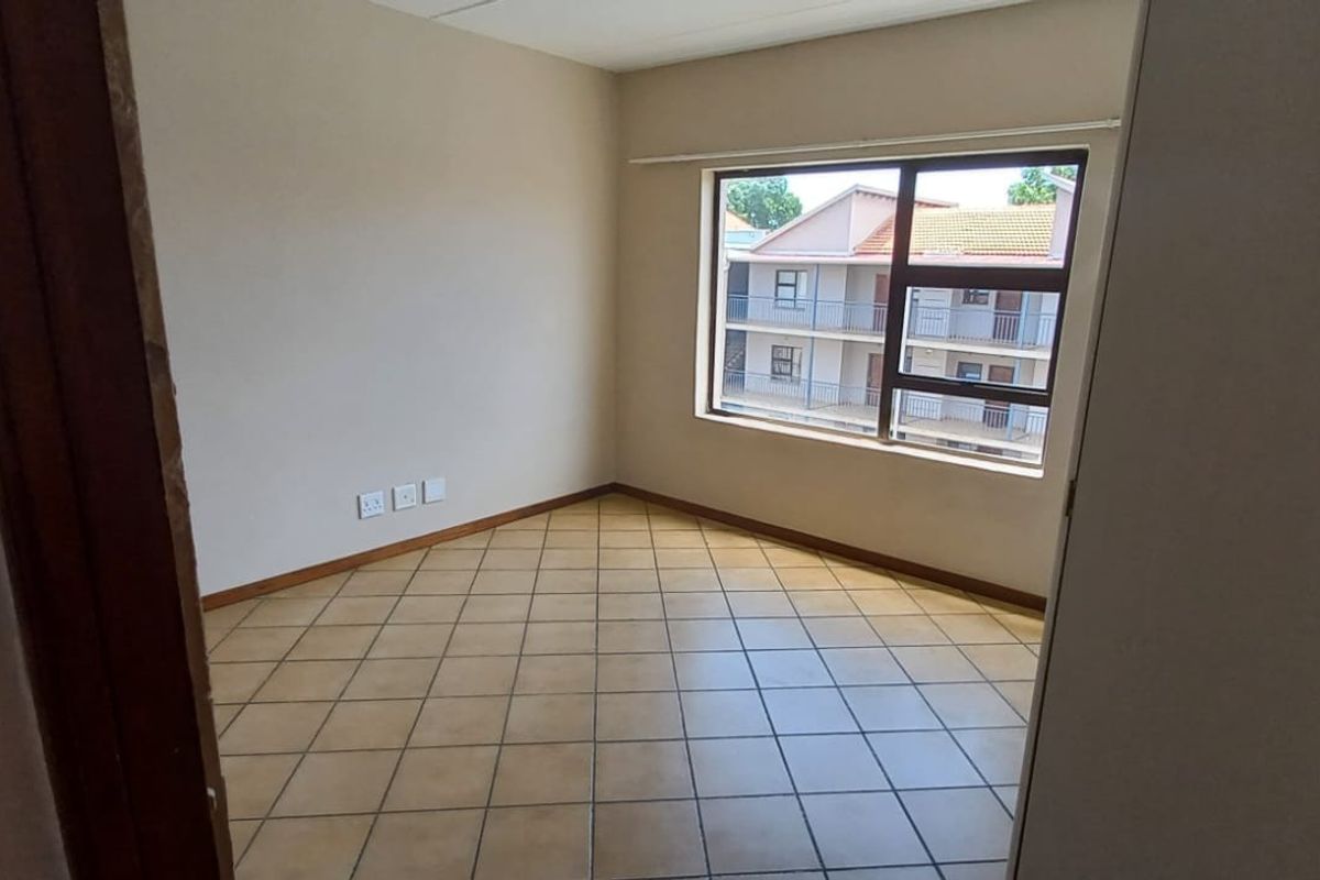 An empty bedroom featuring tiled flooring and a large window with an aluminium frame, offering a neutral space ready for personalization.