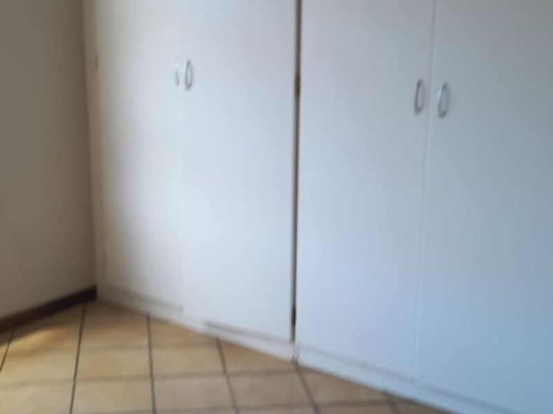 An empty bedroom featuring tiled flooring and built-in cupboards with white doors.