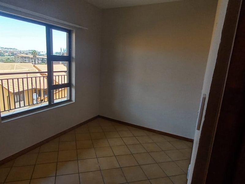 A bright, empty bedroom featuring tiled flooring and a large window with views of the surrounding complex.