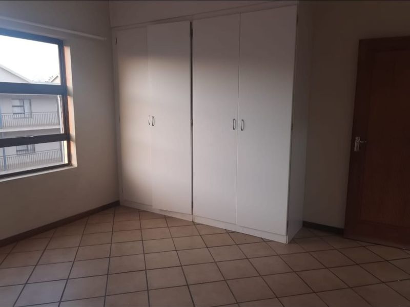 A vacant bedroom featuring built-in cupboards, tiled flooring, and a large window providing natural light.