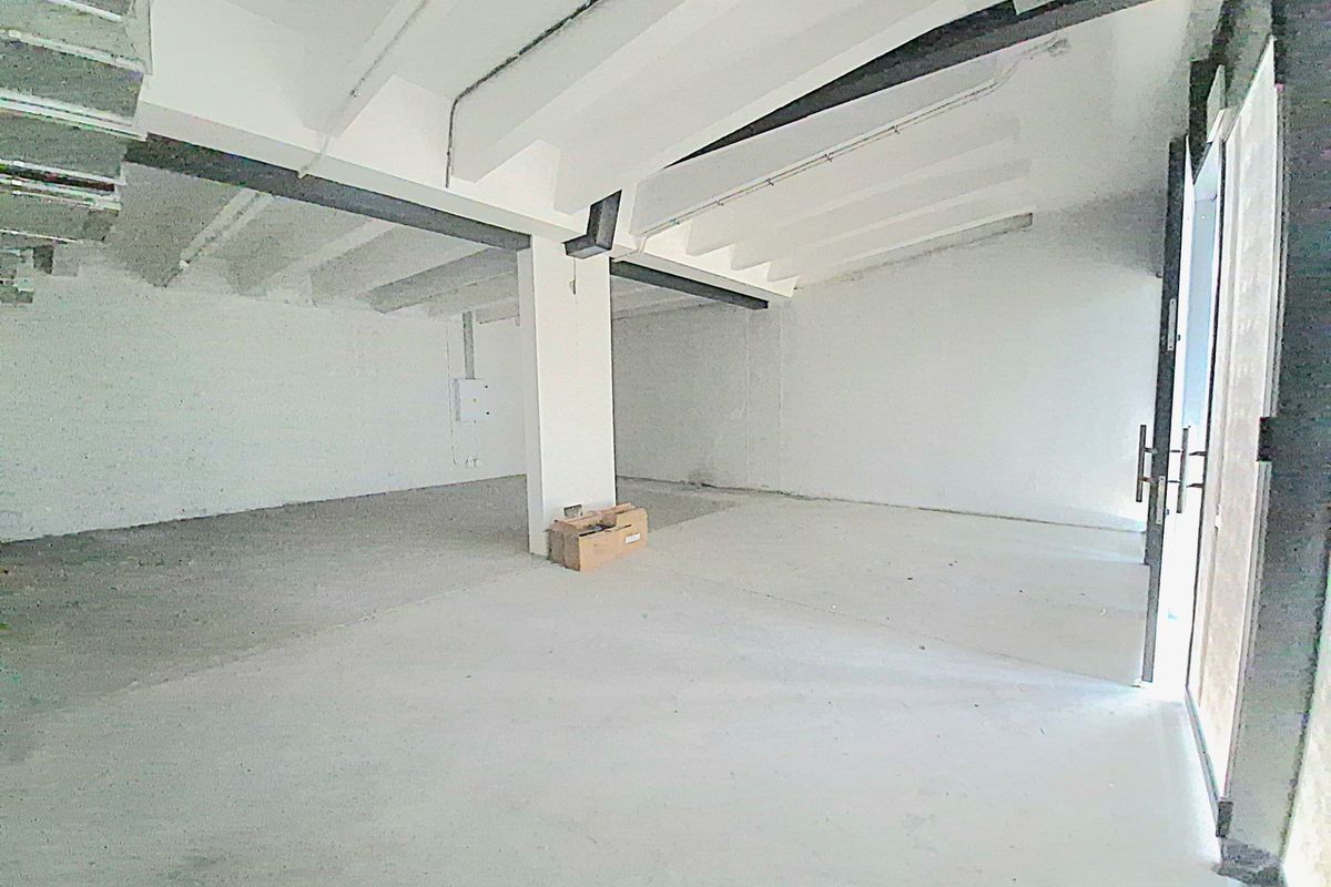 An empty, unfinished open-plan retail space featuring exposed concrete ceilings, structural columns, and a glass entrance door, ready for custom fit-out.