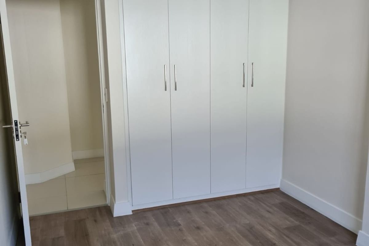 A clean, empty bedroom featuring modern laminate flooring, neutral walls, and ample built-in cupboard storage.