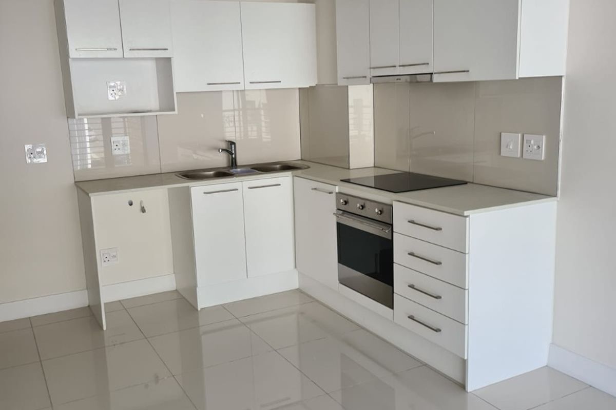 Modern, clean-lined kitchen featuring white cabinetry, integrated electric hob, oven, extractor fan, and polished tiled flooring in an open-plan layout.