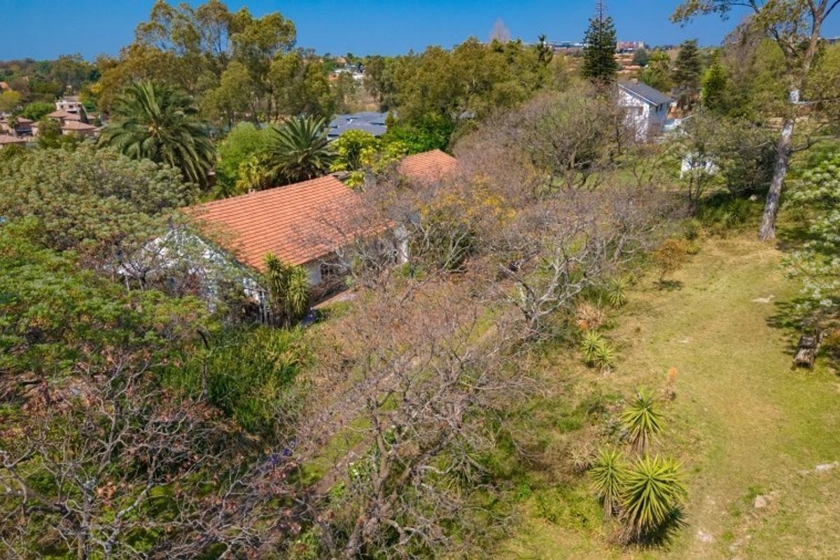 An aerial view of the property showcasing the house with a terracotta tiled roof set within a large, mature garden with established trees.