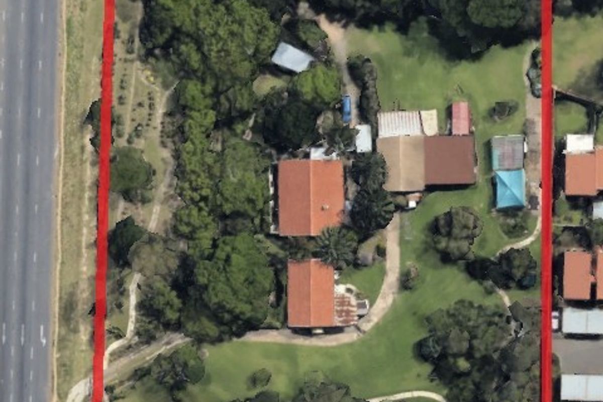 Aerial view of a large residential property featuring multiple structures, mature trees, and extensive garden space situated along a main road.