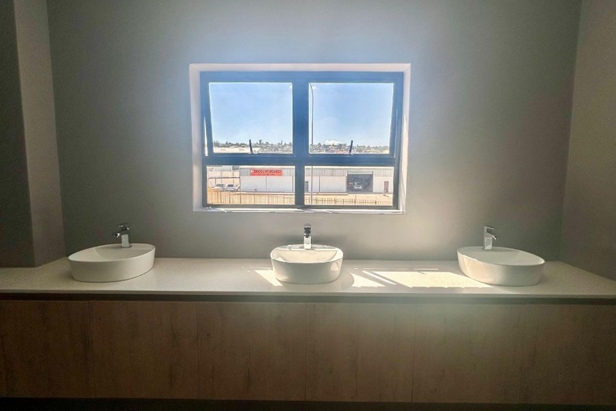 Modern commercial bathroom featuring a triple vessel sink vanity with stone countertop and timber cabinetry, set against a neutral grey wall.