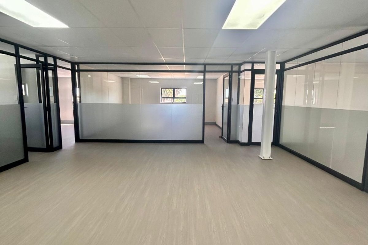 Modern open-plan office space featuring glass partitions, suspended ceilings with recessed lighting, and durable vinyl flooring, offering a clean and professional work environment.