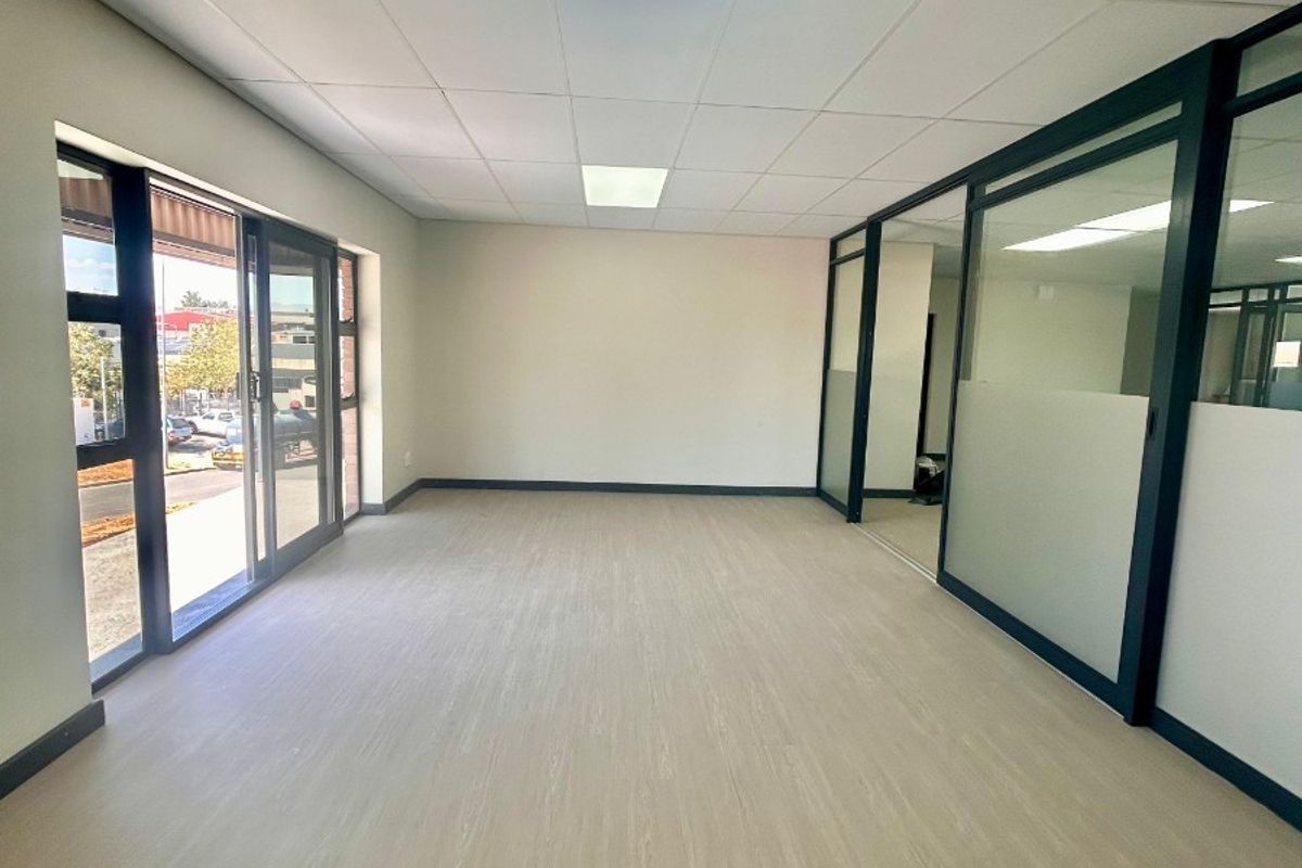 A bright, modern, and empty office space featuring glass partition walls, suspended ceilings with recessed lighting, and durable vinyl flooring.