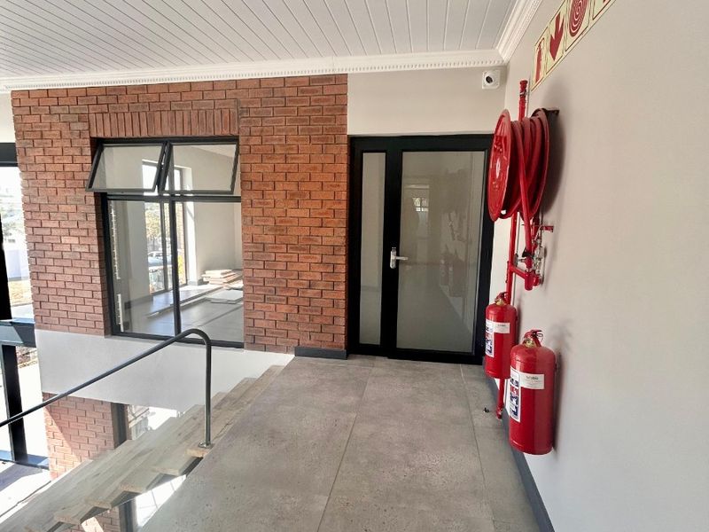 A modern hallway featuring exposed brickwork, tiled flooring, and essential fire safety equipment, including a hose reel and extinguishers.