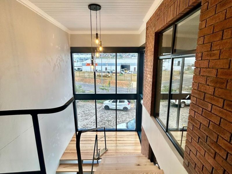 A bright, modern staircase area featuring timber treads, an exposed brick feature wall, and large windows providing natural light and exterior views.