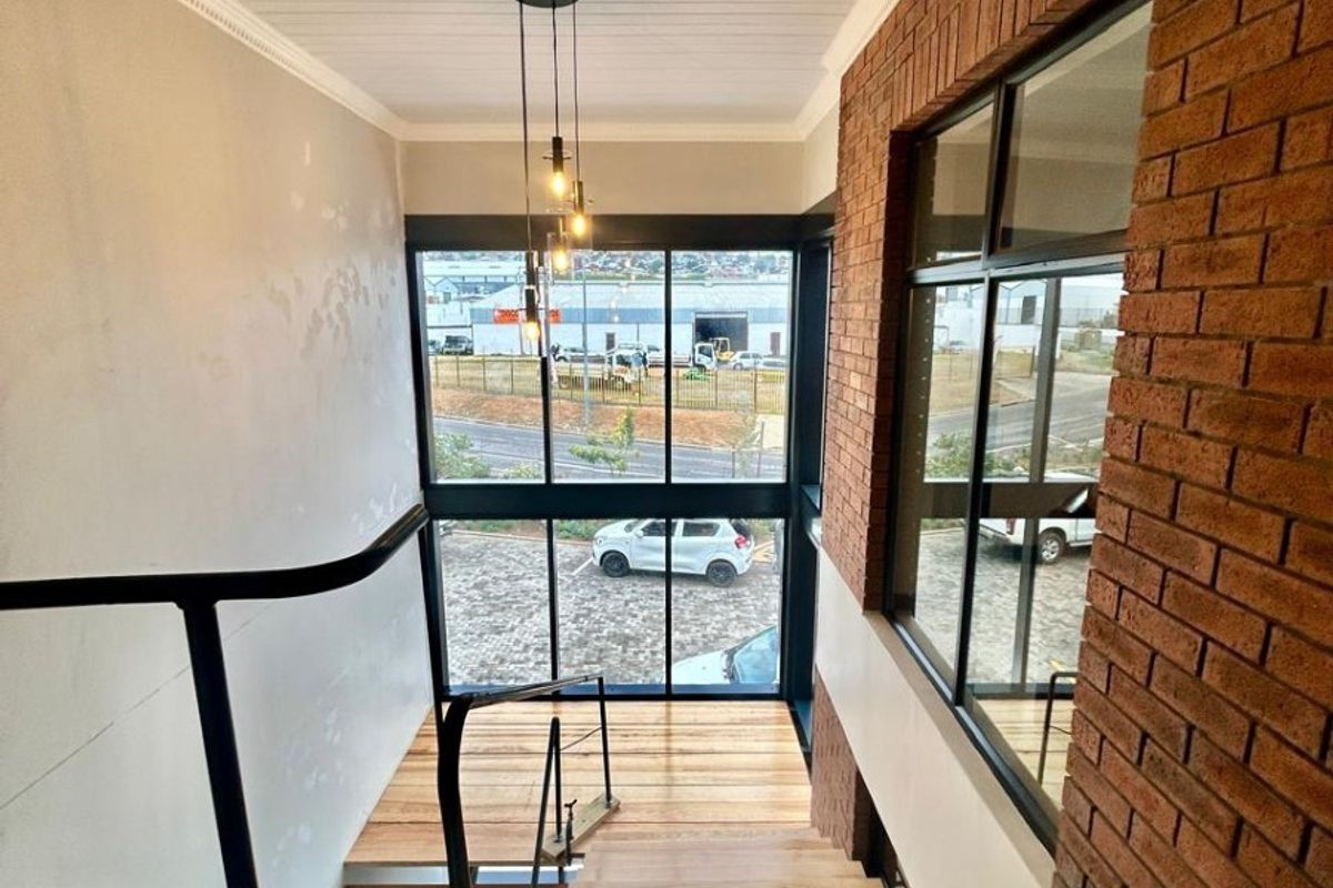 A bright, modern staircase area featuring timber treads, an exposed brick feature wall, and large windows providing natural light and exterior views.