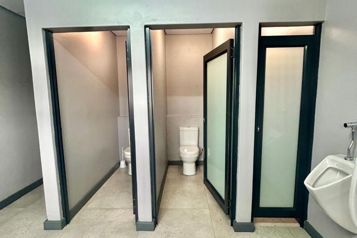 Commercial bathroom facility featuring multiple toilet cubicles, a wall-mounted urinal, and modern tiled flooring.