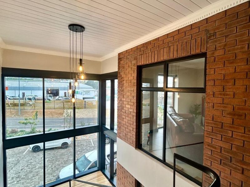 Modern double-volume hallway featuring a timber staircase, exposed brick feature wall, and expansive floor-to-ceiling windows providing ample natural light.