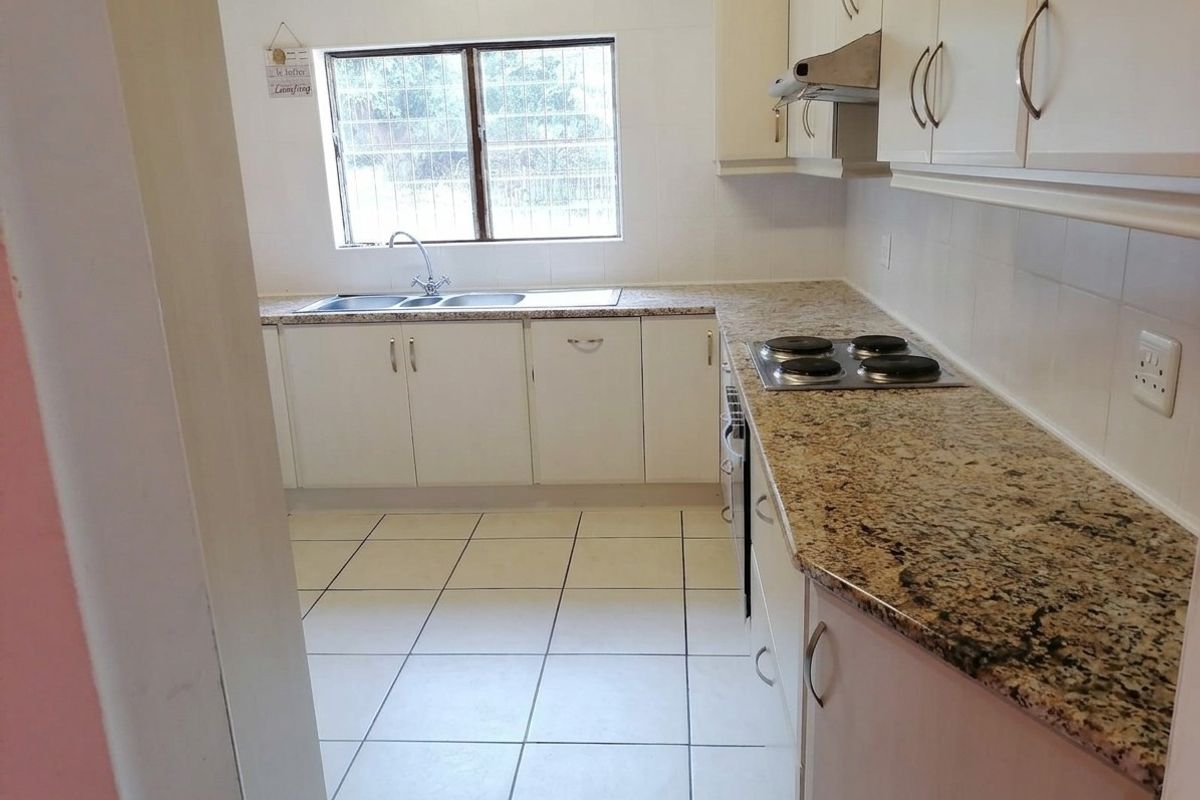 A functional kitchen featuring granite countertops, white cabinetry, an electric hob with extractor fan, and tiled flooring.