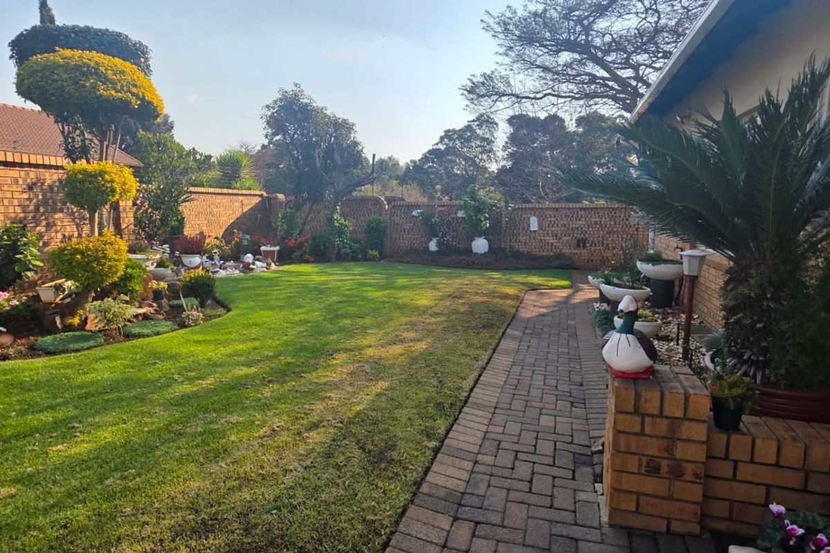 A well-maintained rear garden featuring a lush green lawn, paved walkway, and established brick boundary walls.