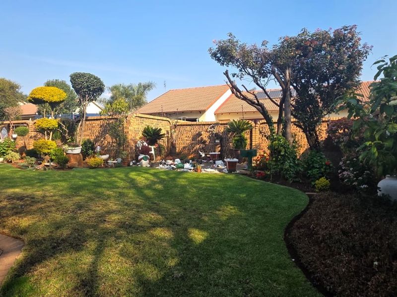 A well-maintained residential garden featuring a manicured lawn, established trees, and a perimeter brick boundary wall.