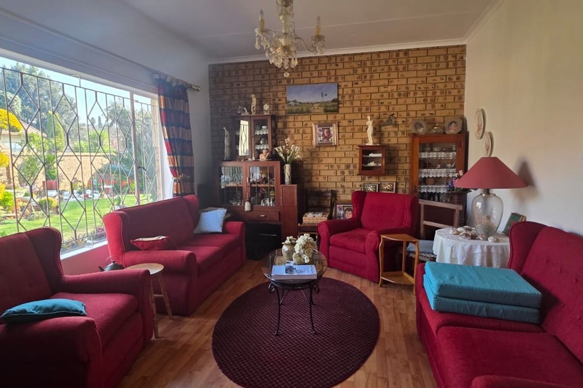A spacious living room featuring an exposed brick accent wall, laminate flooring, and a large window overlooking the garden.