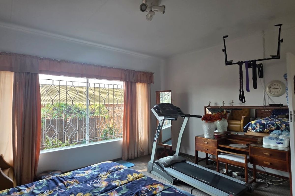 A bedroom featuring a large window with security bars, neutral walls, and a ceiling-mounted light fixture.