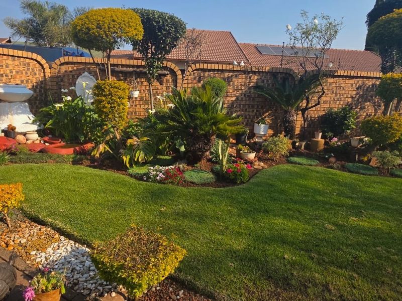 A well-maintained private garden featuring a manicured lawn, established garden beds, and a secure brick boundary wall.