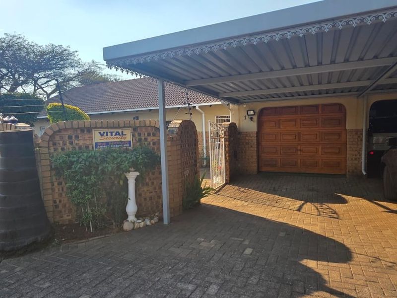 Front exterior view featuring a paved driveway, covered carport, wooden garage door, and secure brick boundary wall with electric fencing.