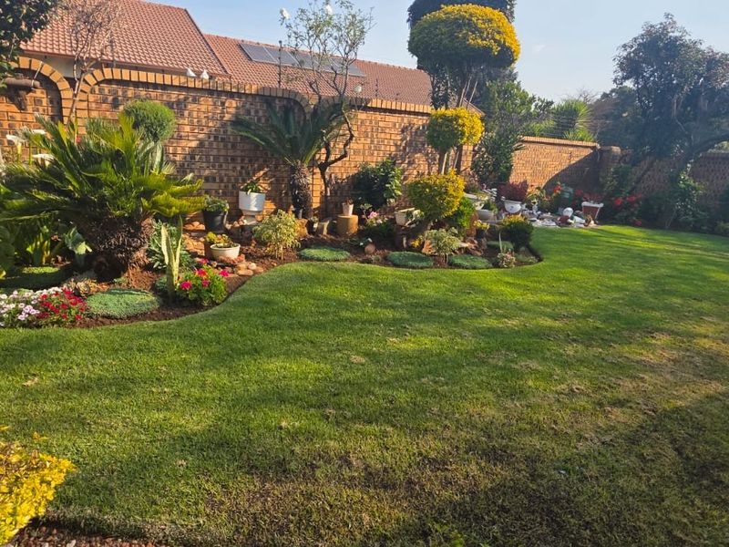 A well-maintained private garden featuring a lush green lawn, landscaped garden beds, and a secure brick boundary wall.