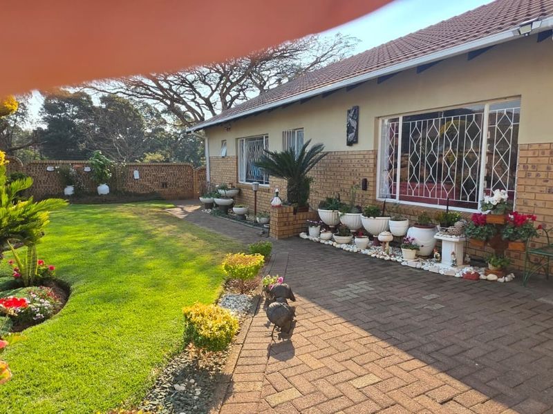 A view of the rear garden featuring brick paving, a well-maintained lawn, and the rear facade of the house with security bars on windows.