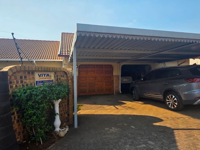 Front exterior view of the property featuring a paved driveway, a covered carport, and a secure garage entrance with brick boundary walling.