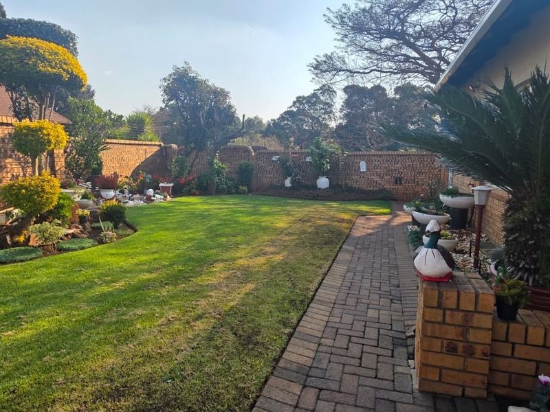 A well-maintained rear garden featuring a lush green lawn, paved walkway, and established brick boundary walls.