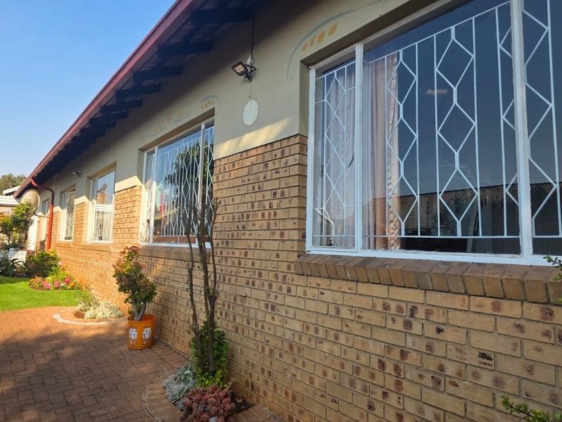 A well-maintained rear exterior view of the house featuring a face brick facade, paved walkway, and secure window bars.