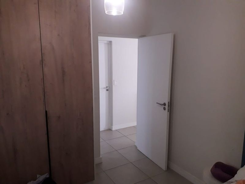 A bedroom interior featuring tiled flooring, a built-in wood-finish wardrobe, and a doorway leading to an adjacent hallway.