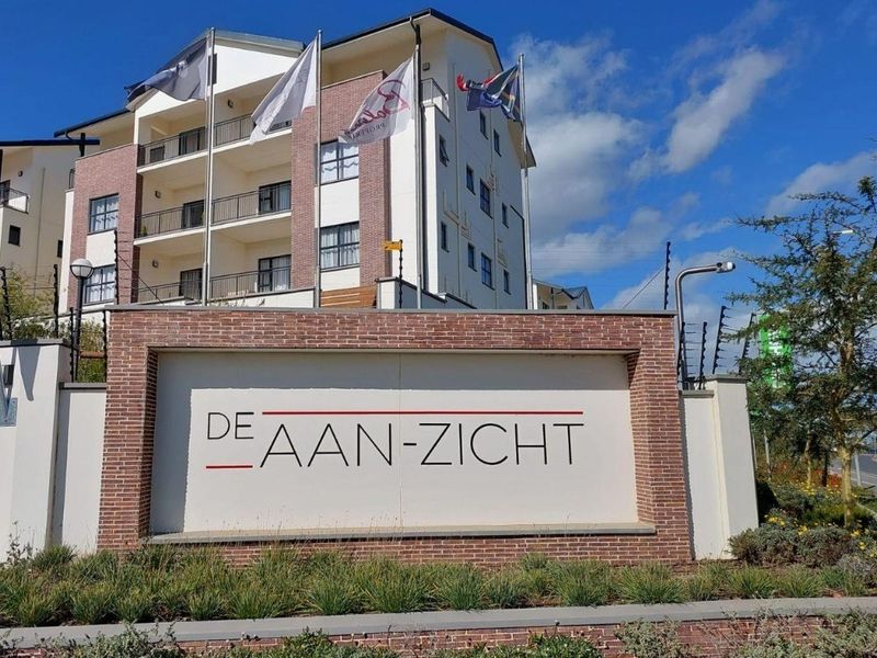 Front entrance view of the De Aan-Zicht apartment complex, featuring a brick boundary wall, electric fencing, and modern multi-story residential architecture.