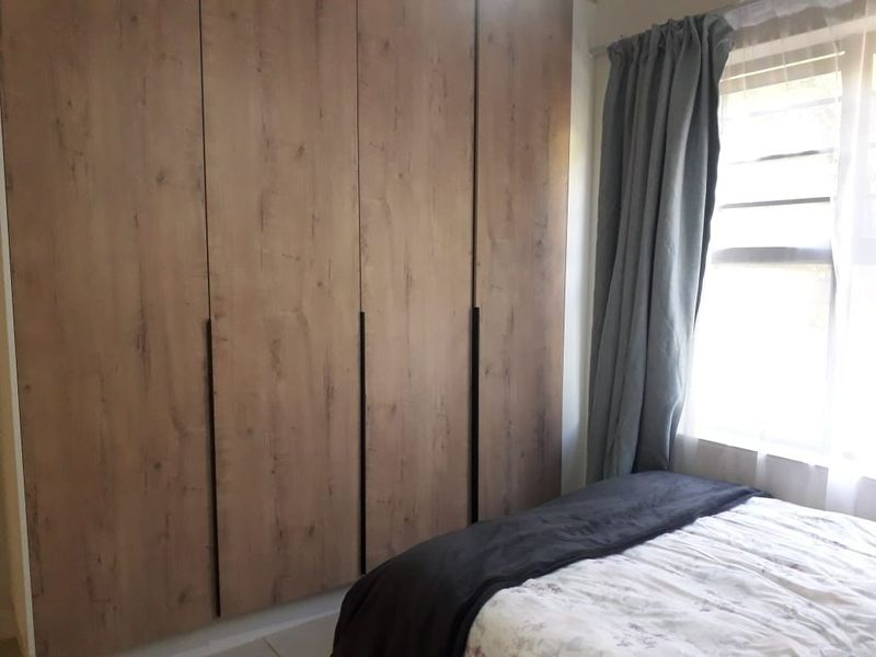 A bedroom featuring modern wood-finish built-in cupboards and a window with curtains.