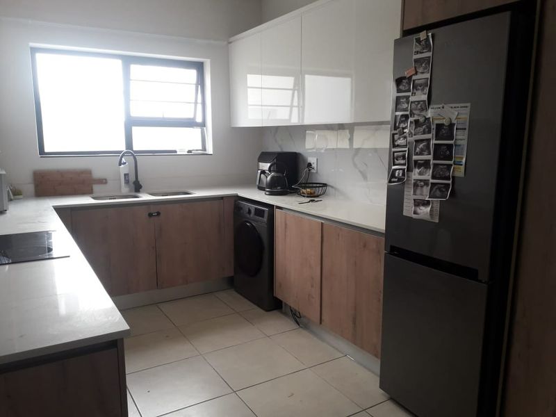 Modern kitchen featuring sleek wood-tone and white cabinetry, quartz countertops, a double sink, and integrated appliance space with tiled flooring.