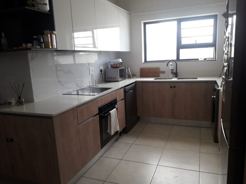 Modern kitchen featuring wood-grain and white cabinetry, stone countertops, marble-effect splashback, integrated oven, and hob with tiled flooring.