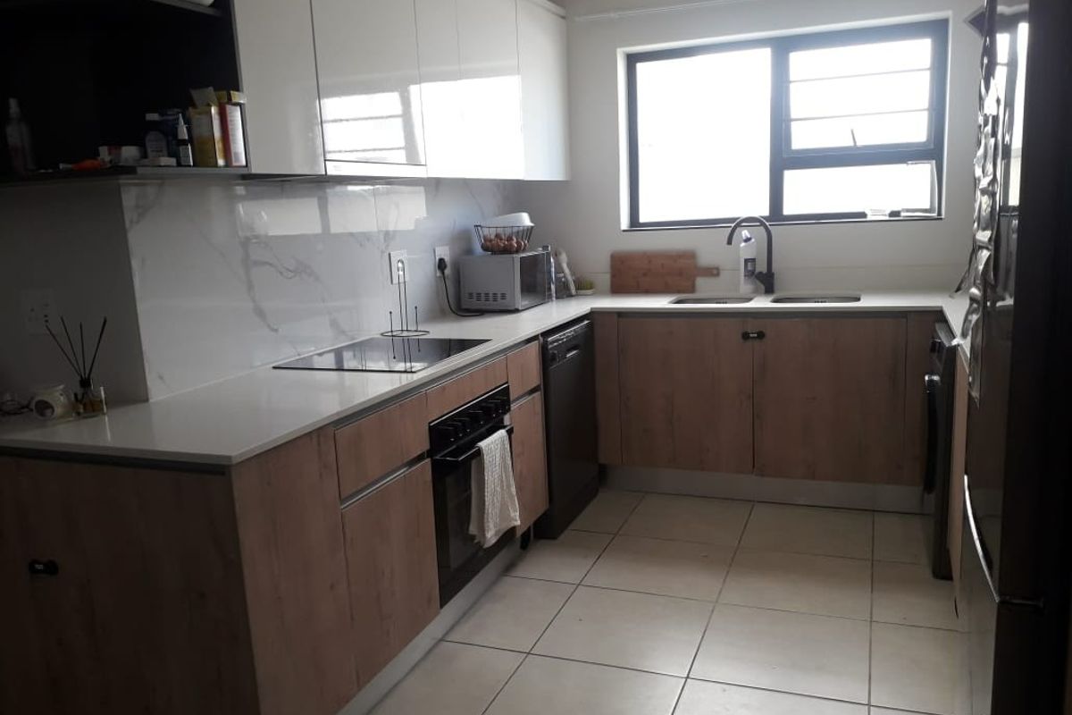 Modern kitchen featuring wood-grain and white cabinetry, stone countertops, marble-effect splashback, integrated oven, and hob with tiled flooring.