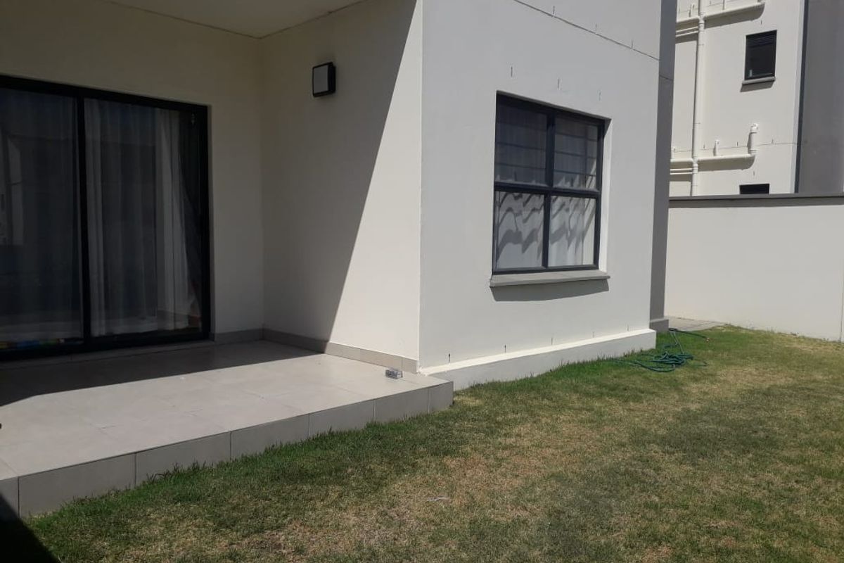 Rear view of the apartment featuring a tiled patio area, sliding glass doors, and a private garden space with boundary wall.