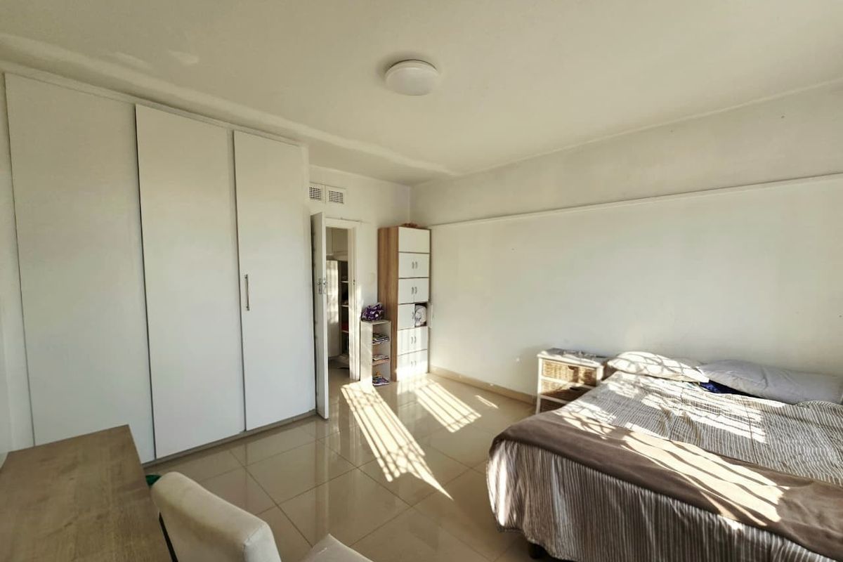 A bright bedroom featuring tiled flooring and ample built-in cupboard storage, offering a clean and functional living space.