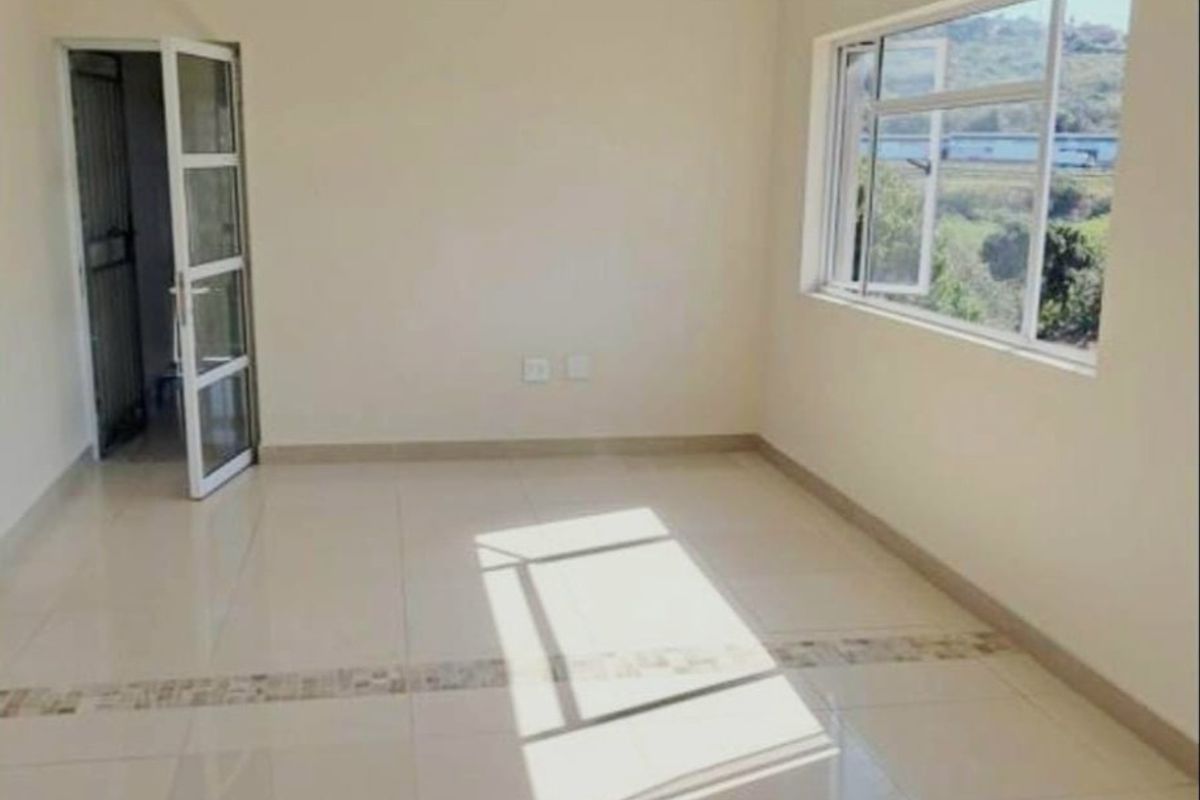 A bright, empty living area featuring neutral tiled flooring, a large window with natural light, and a glass panel door leading to an adjacent space.